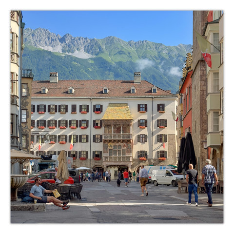 Es ist die Herzog-Friedrich-Straße von Innsbruck zu sehen. Diese führt zum alten Rathaus und über dem Eingang ist das Goldene Dachl zu sehen. Über diesem sieht man die Nordkette, ein Gebirgszug oberhalb von Innsbruck.
Auf der Straße selbst sind einige Menschen zu sehen. Da das Bild am Vormittag aufgenommen wurde, sieht man auch 2 Lieferwagen dort stehen.